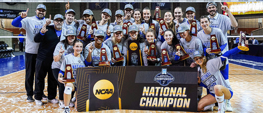 Former D11 volleyball national champions holding banner and trophy