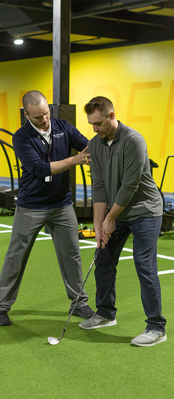 person inside on turf being trained how to golf from a trainer