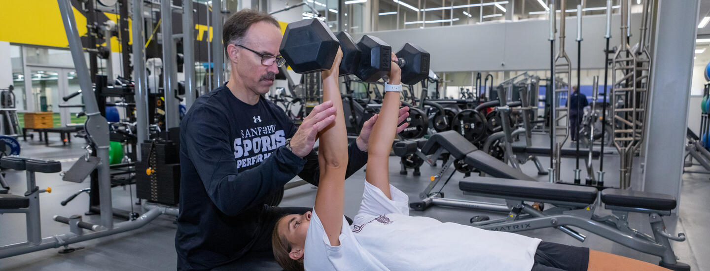 Performance coach assisting girl with dumbbell bench press
