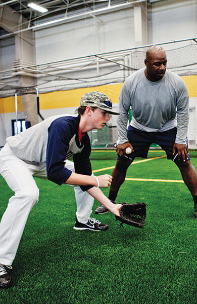 Image of athlete fielding a baseball while receiving instruction from a coach