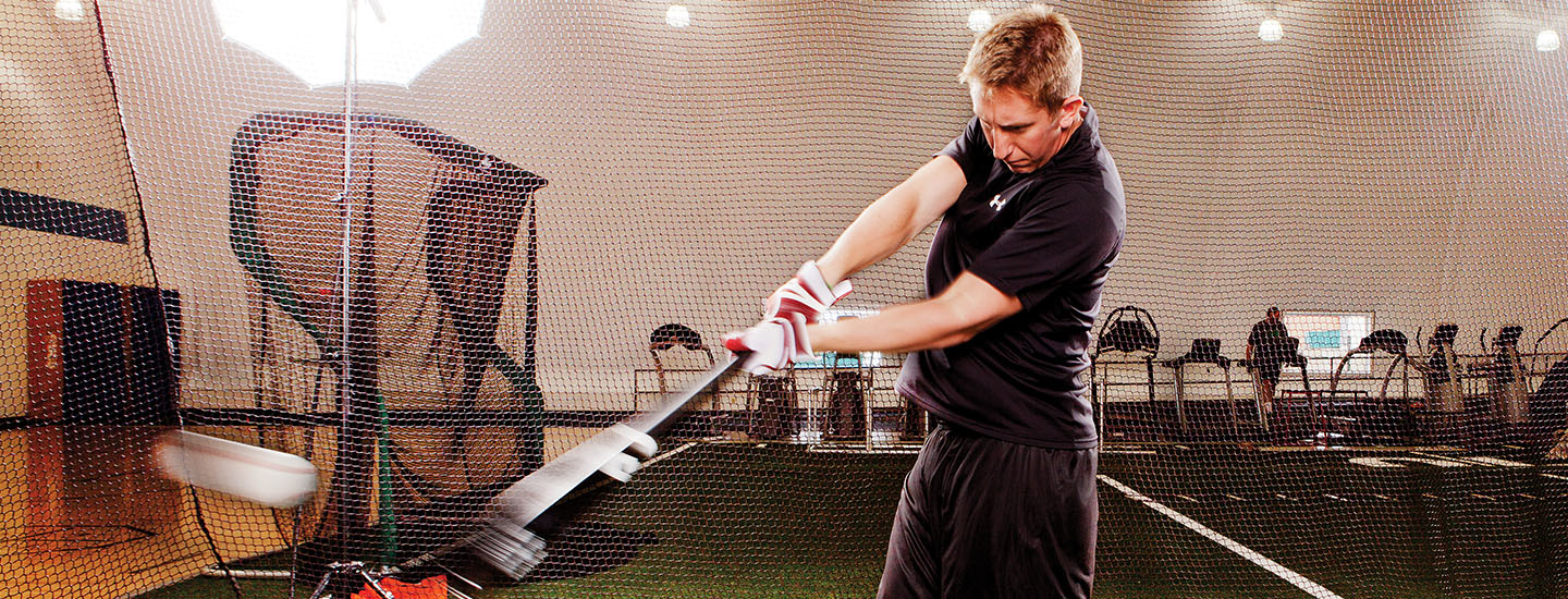 baseball player swinging bat in batting cage