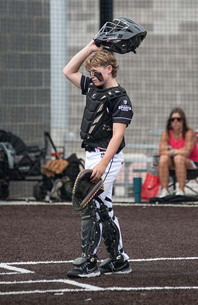 baseball catcher in black jersey standing above home plate taking off his helmet 