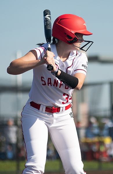 softball player with white and red jersey holding a bat at home plate ready for the pitcher 