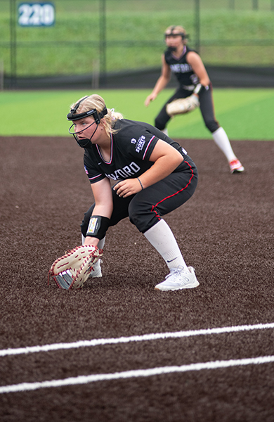 softball player in black jersey crouching to catch ball on the field
