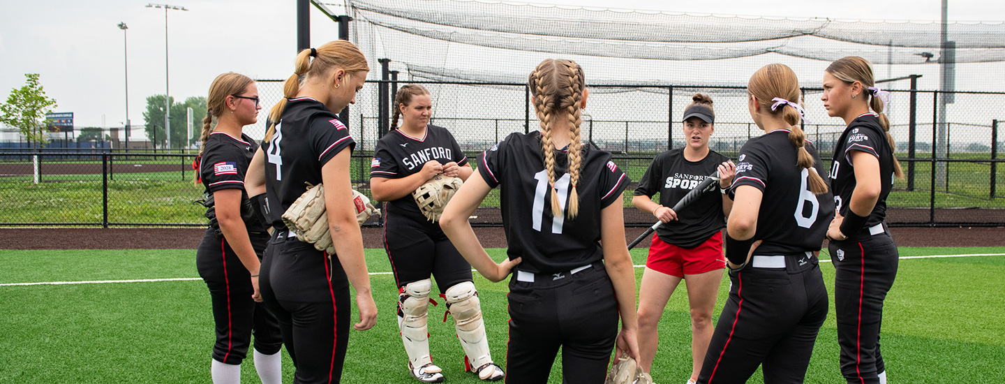 softball team in black and red jerseys huddled in a circle on the field 