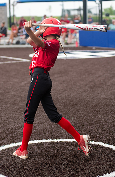 softball player practicing her batting swing outside the dugout 