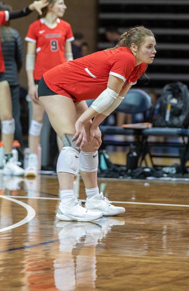 volleyball player on the court wearing red jersey resting her hands on her knees 